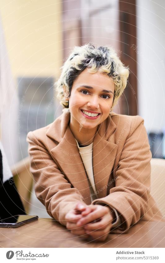 Lächelnde Frau im Mantel am Tisch auf der Straße Café positiv heiter trendy ruhen Terrasse Glück jung sitzen hölzern Kantine genießen modern Freude Kälte