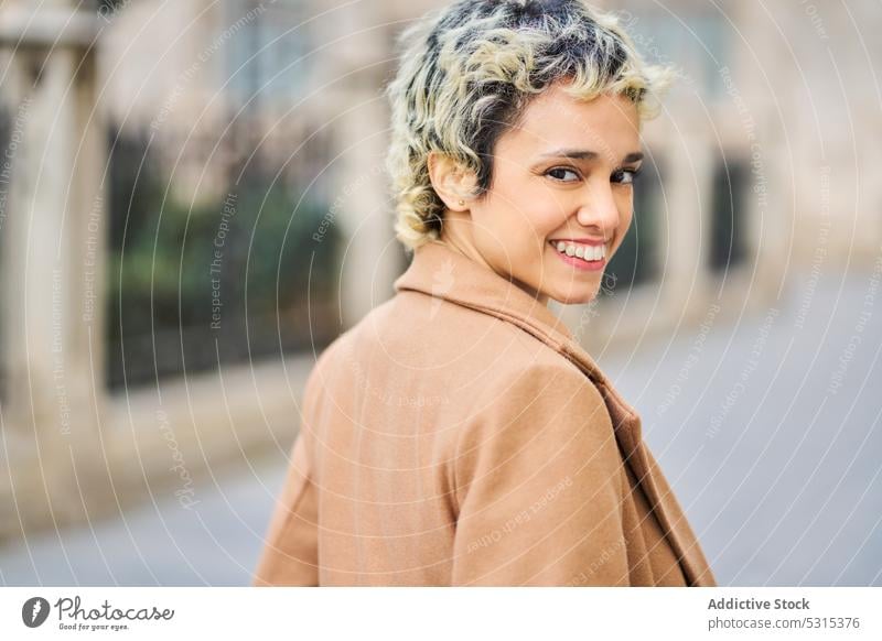 Fröhliche Frau in stilvollem Outfit geht auf dem Bürgersteig Lächeln Spaziergang Gebäude Straße Straßenbelag historisch Stil Großstadt positiv blond trendy jung