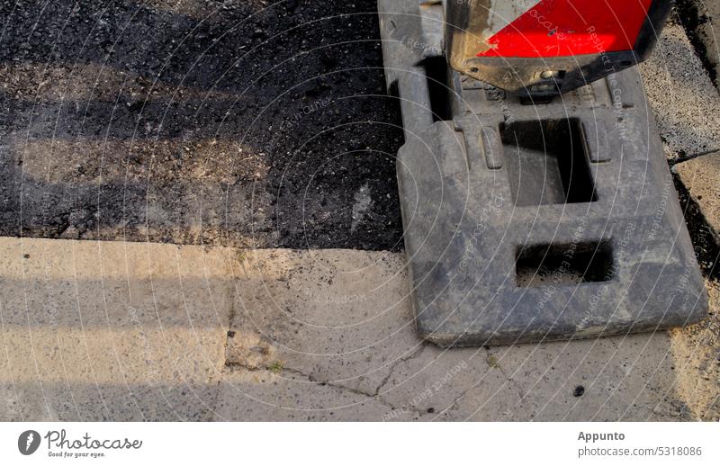 Straßenarbeiten (Hellgraue Asphaltdecke mit einem frisch geteertem dunkleren Streifen und Ausschnitt einer rot-weißen Warnbake) Teer Straßenbelag Straßenbake