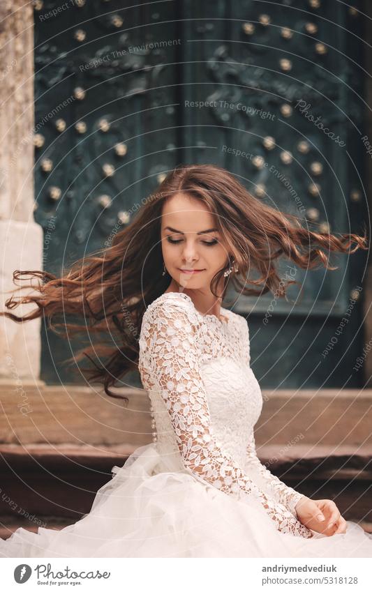 Porträt einer schönen jungen Braut in einem weißen Hochzeitskleid mit langen Haaren in der alten europäischen Stadt. Frau in der Nähe von alten Gebäude. Hochzeitstag