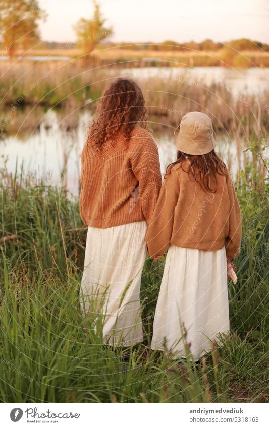 Muttertag. Rückenansicht der jungen Mutter mit kleinen Mädchen stehen in der Nähe von See, Teich am Sommertag. Familie genießt das Leben zusammen. Mutter und Kind Tochter verbringen freie Zeit im Freien. Familie schauen.