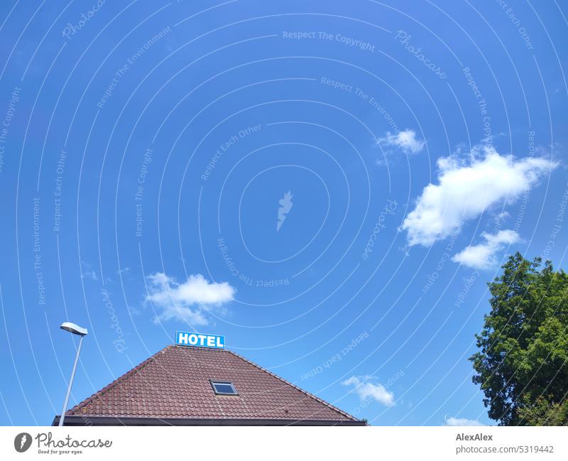 Ziegeldach mit HOTEL- Schild vor blauem Himmel Hotel Dach Fenster Dachfenster Laterne Straßenlaterne Baum blauer Himmel Schönes Wetter Luft Wolken Außenaufnahme