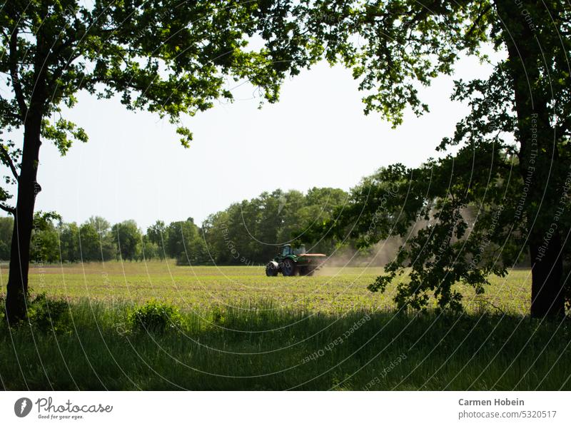 Ein fahrender Trecker auf einem bestellten Feld mit im Wachstum befindlichen grünen Pflanzen eingerahmt von Bäumen