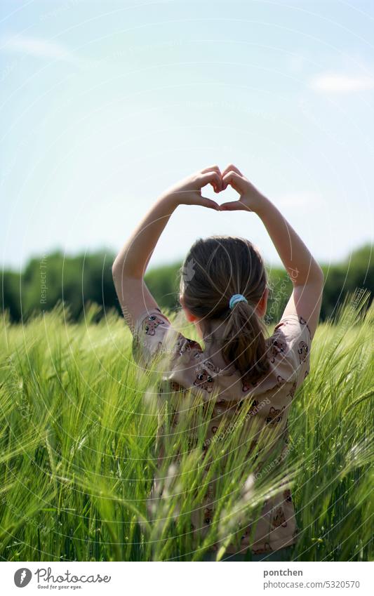 ein kind steht im weizenfeld und formt ein herz mit ihrer hand. landleben liebe kindheit landeben landliebe kornfeld Weizen Weizenfeld Landwirtschaft