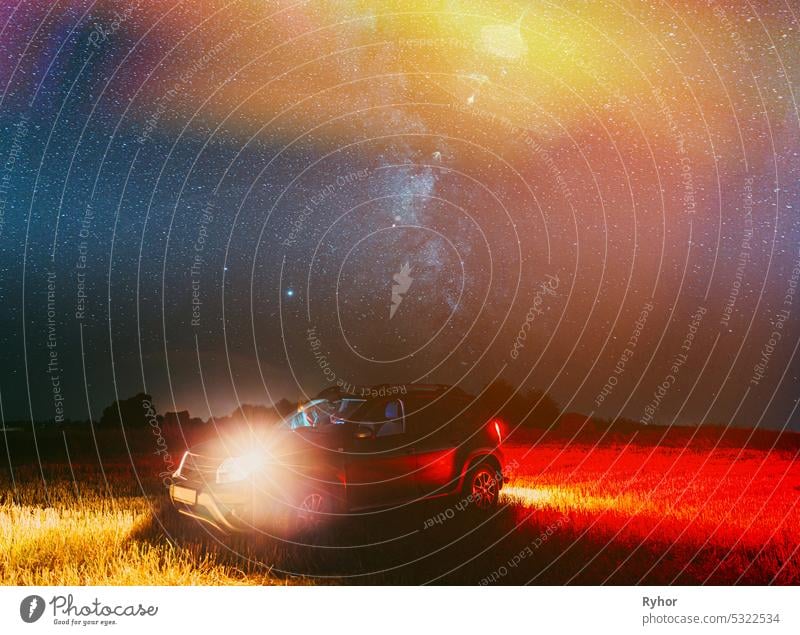 Landwirtschaftlichen bunten Hintergrund kopieren Raum. Night Starry Sky Above Rural Landscape With Suv Parked On Field Meadow After Harvest. Glühende Sterne und Sonnenuntergang Lichter