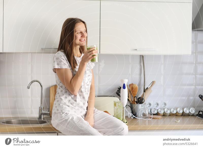 Schönes Mädchen trinkt frisch zubereiteten Smoothie in der Küche. Smoothies frisch aus verschiedenen pflanzlichen Zutaten auf Küchentisch gemacht. Gesundes Essen. selektiver Fokus