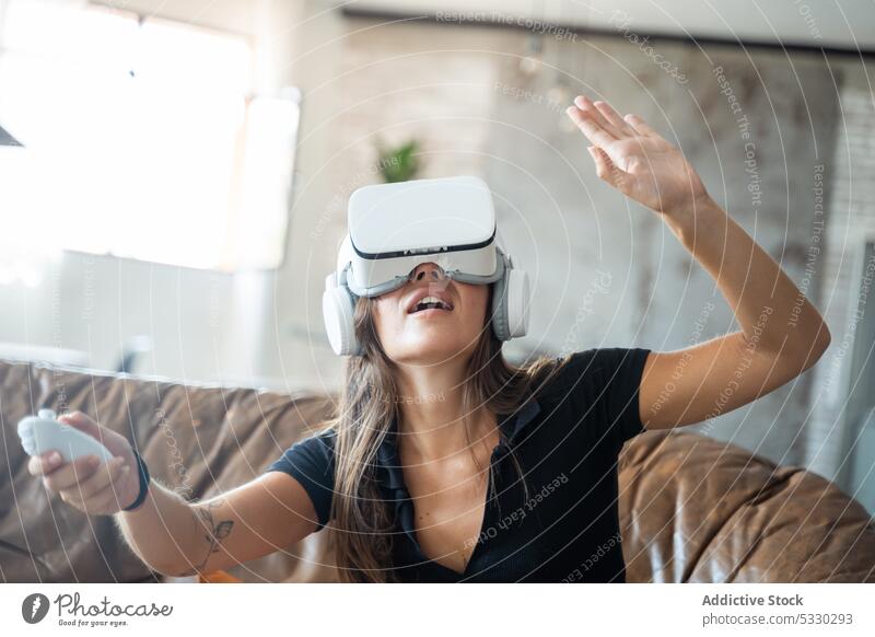 Frau in VR-Headset interagiert mit digitaler Welt mithilfe von Controllern Videospiel interagieren spielen Regler Virtuelle Realität Sofa heimwärts Erfahrung