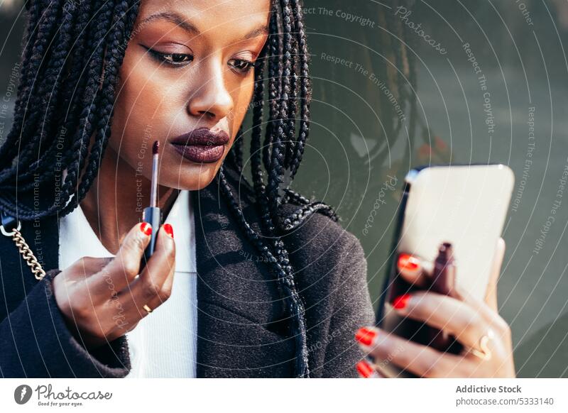 Schwarze Frau trägt auf der Straße Lippenstift auf Smartphone bewerben Make-up benutzend Geflecht Gerät Mobile Gesicht Afroamerikaner ethnisch schwarz Afro-Look