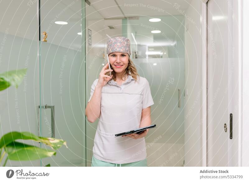 Lächelnder Arzt, der in der Klinik mit seinem Smartphone spricht sprechen Frau reden Arbeit Tablette Spezialist Uniform Krankenhaus Gerät medizinisch positiv