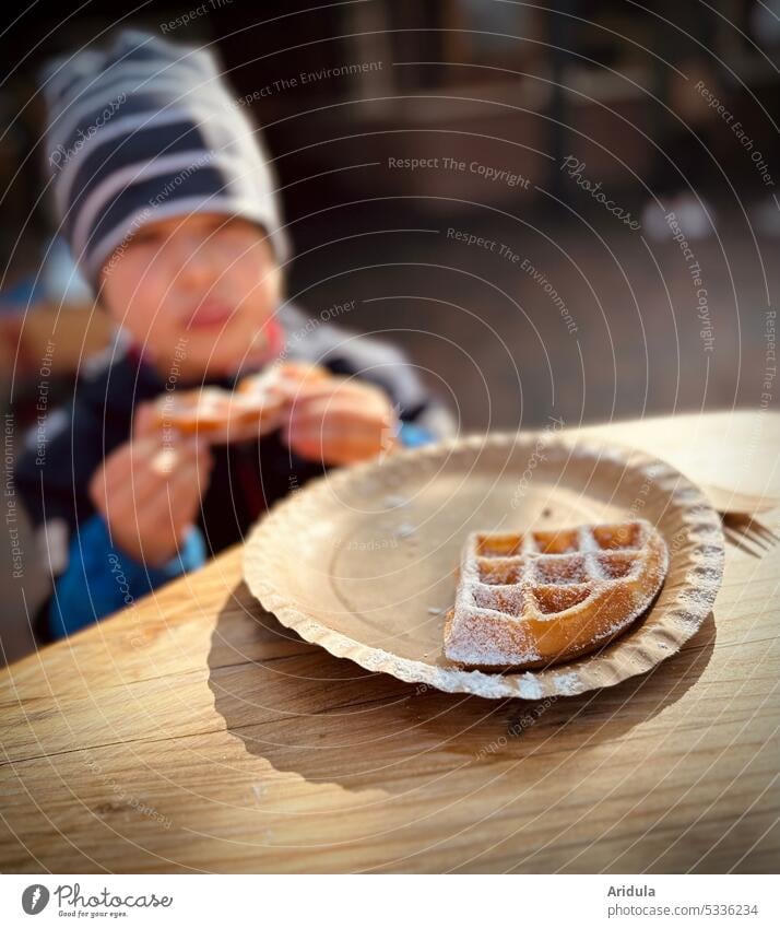 Teller mit Waffel und Puderzucker, im Hintergrund ißt ein Kind ein Stück Waffel süß lecker Ernährung Lebensmittel Süßwaren Backwaren Essen Zucker Kuchen