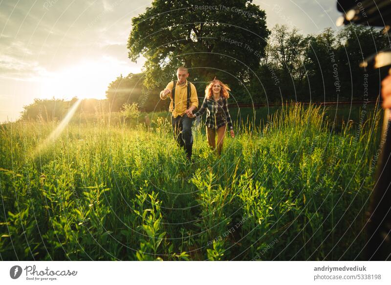 Verliebtes Hipster-Paar, das im Feld spazieren geht, sich küsst und die Hände hält, sich umarmt, im Sommer bei Sonnenuntergang im Gras liegt. valentines day