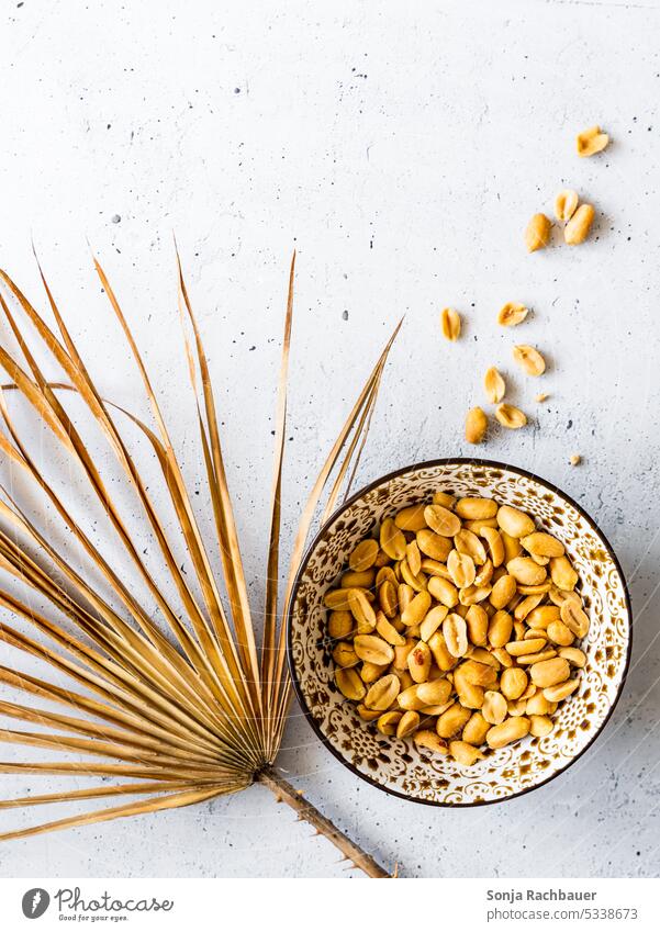 Geröstete und gesalzene Erdnüsse in einer Schüssel auf einem rustikalen grauen Tisch. Draufsicht. geröstet Knabbereien salzig Snack Palmblatt knackig essen