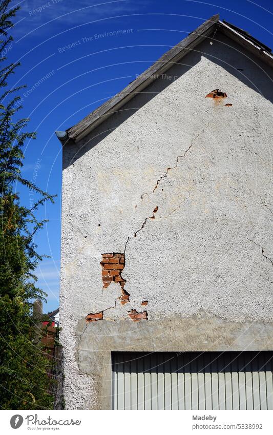 Alte Fassade eines Wohnhaus mit bröckelndem Putz, Spitzgiebel und Garage vor blauem Himmel im Sonnenschein in Wettenberg Krofdorf-Gleiberg bei Gießen in Hessen