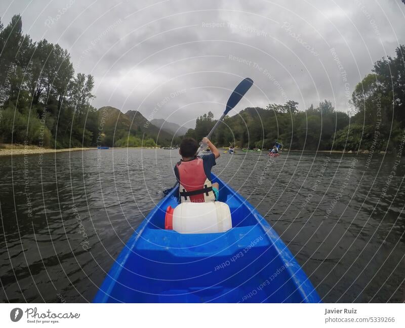 ein junger Kanufahrer, von hinten gesehen, paddelt in einem Kajak auf einem breiten Fluss, andere Kanufahrer sind im Hintergrund unscharf, Abfahrt des Flusses Sella