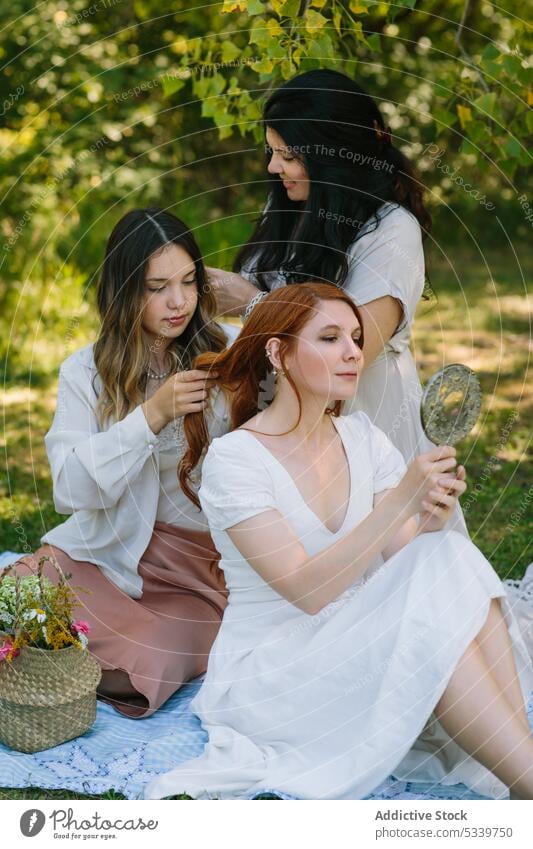 Ruhige Frauen, die sich im Park gegenseitig frisieren Picknick Sommer Freund Zusammensein Rasen Frisur Wiese Gras Freundschaft Decke Natur Wochenende Glück