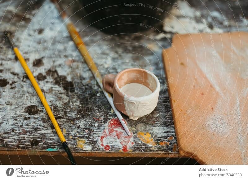 Tontopf neben Pinseln in schäbiger Werkstatt Tasse Gerät Pinselblume Handwerk Tisch Töpferwaren dreckig Kunst kreativ Hobby Atelier Werkzeug Grunge Fähigkeit