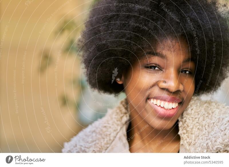 Glückliche ethnische junge Frau mit Afrofrisur Lächeln Afro-Look Porträt positiv heiter froh lange Haare gemütlich Optimist Vorschein Dame Zahnfarbenes Lächeln