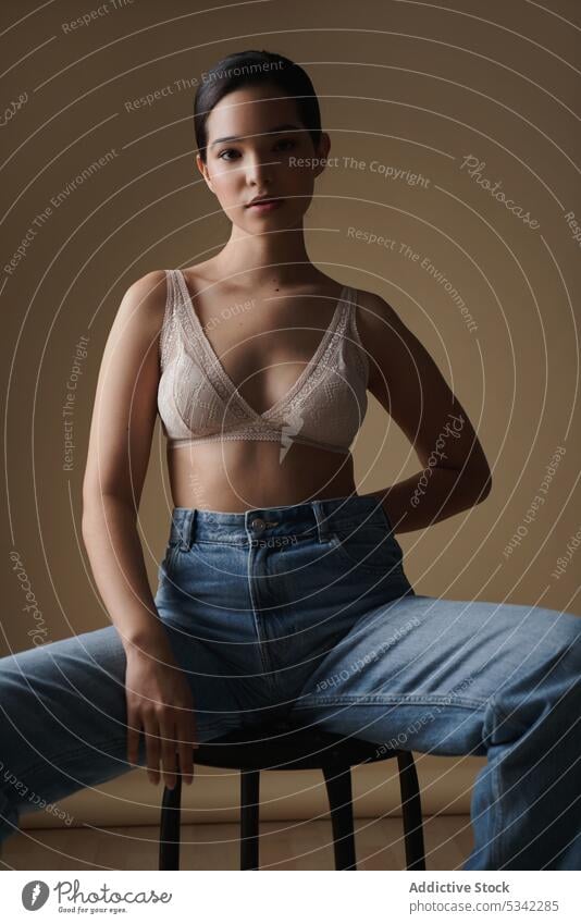 Anmutige Frau sitzt auf einem Stuhl in einem hellen Studio Stil Dessous Porträt Model nachdenklich sinnlich Hocker Jeanshose Unterwäsche Figur Atelier