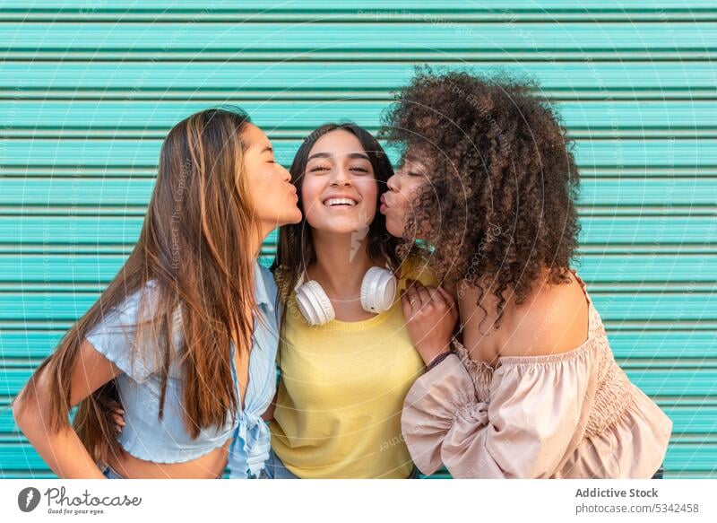 Glückliche verschiedene Frauen küssen Freund Wangen Kuss Freundin Zusammensein Lächeln Freundschaft heiter bester Freund Partnerschaft rassenübergreifend