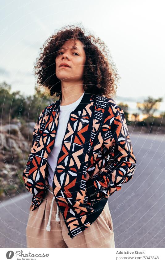 Stilvolle ethnische Frau steht auf der Straße Hand-in-Tasche Individualität Ornament Muster krause Haare selbstbewusst Vorschein Erwachsener Outfit Streetstyle