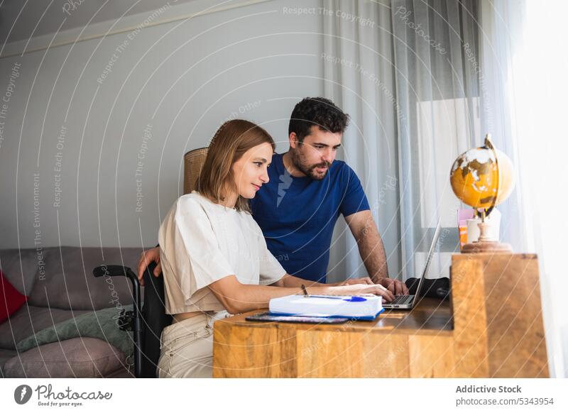 Junges Paar arbeitet zu Hause gemeinsam an einem Büroprojekt Laptop benutzend rollstuhl Reha deaktiviert Hilfsbereitschaft Glück Zusammensein Arbeit Projekt