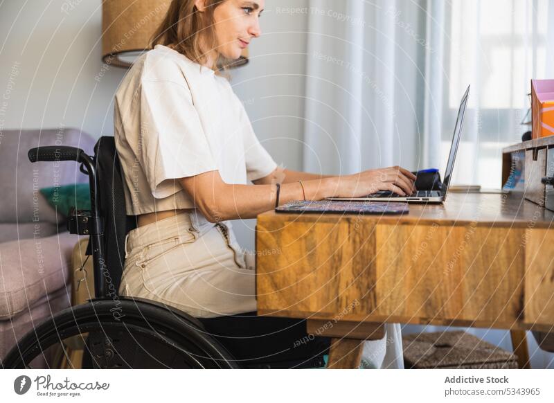 Junge Frau sitzt im Rollstuhl und macht sich Notizen am Laptop Notebook zur Kenntnis nehmen schreiben freiberuflich Sofa Wohnzimmer heimwärts benutzend