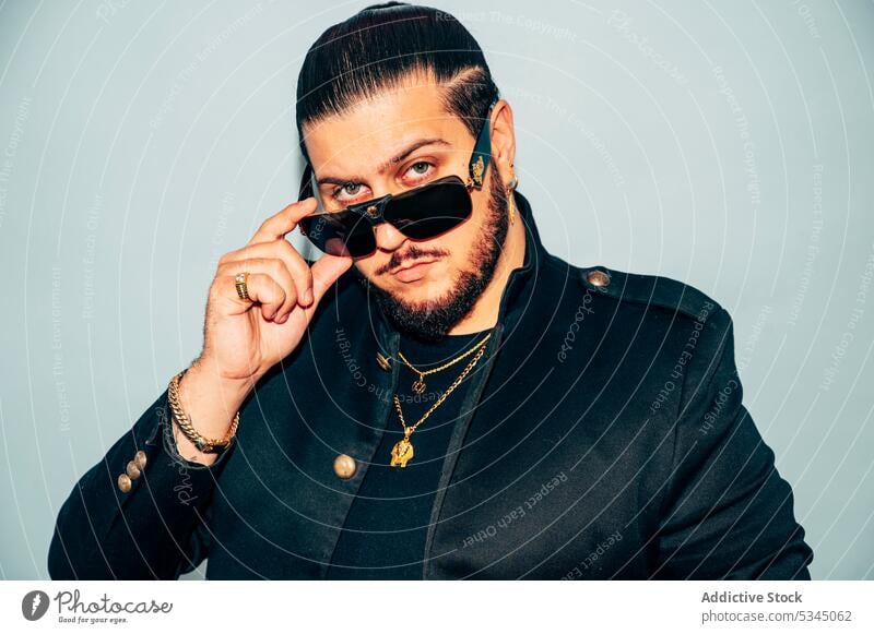 Selbstbewusster Mann, der eine Sonnenbrille vor blauem Hintergrund berührt Mode Stil cool Model Porträt Jacke trendy Vorschein Accessoire männlich Haarschnitt