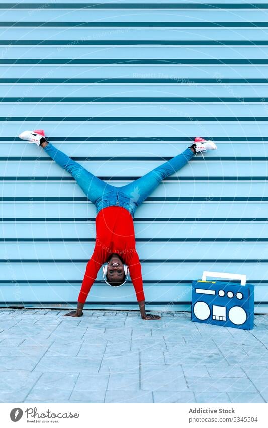 Optimistische junge Frau auf der Straße auf den Armen stehend Handstand Kopfhörer zuhören Musik Boombox Split Lächeln schwarz Afroamerikaner flippig Gesang