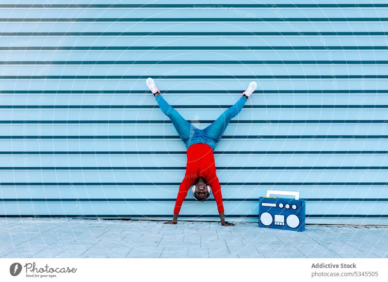 Optimistische junge Frau auf der Straße auf den Armen stehend Handstand Kopfhörer zuhören Musik Boombox Split Lächeln schwarz Afroamerikaner flippig Gesang