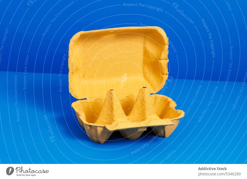 Generative AI-Illustration von leeren gelben geöffneten Karton Eierbehälter auf hellblauem Hintergrund platziert, die Konzept der Recycling-Verpackung Container