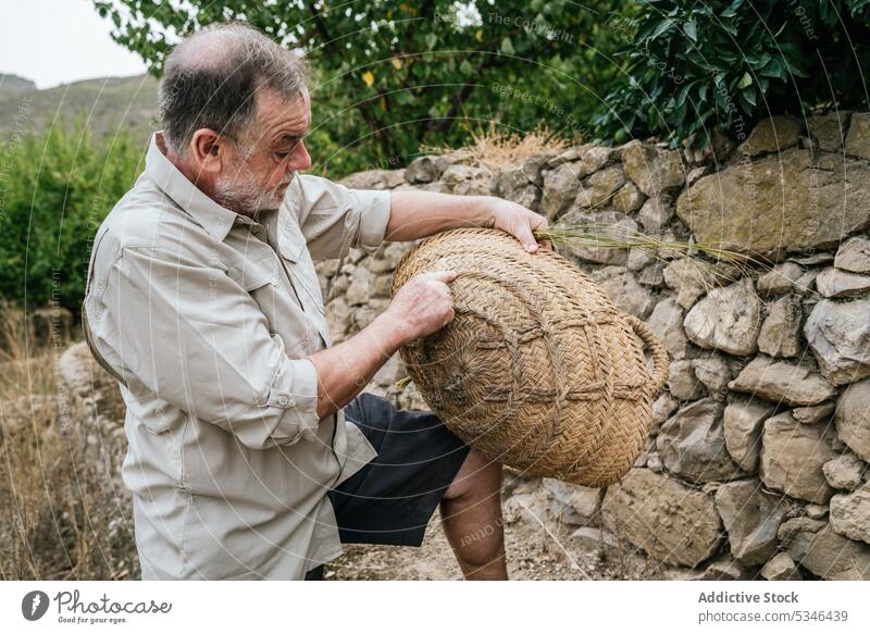 Seriöser reifer männlicher Handwerker prüft Weidenkorb auf dem Bauernhof Mann Korb esparto Gras Landschaft untersuchen Konzentration Kunstgewerbler Meister