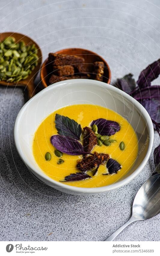 Schüssel mit Kürbiscremesuppe mit Basilikumkräutern auf dem Tisch Schalen & Schüsseln farbenfroh Rahmsuppe cremig knusprig Entzug Diät Abendessen Essgeschirr