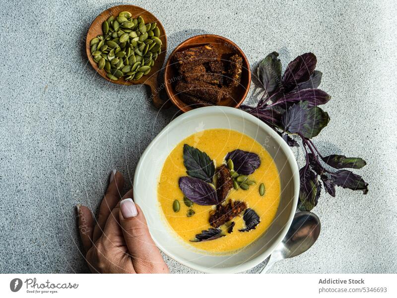 Cropped Hand berühren Schüssel mit Kürbiscremesuppe mit Basilikum Kraut auf dem Tisch Frau Schalen & Schüsseln Rahmsuppe farbenfroh cremig knusprig Entzug Diät