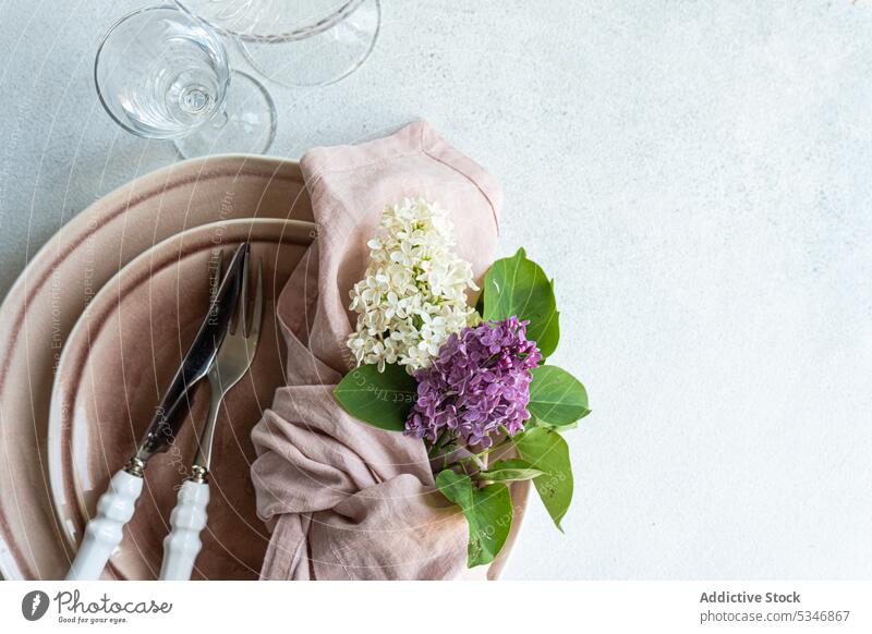 Abgeschnittener Tisch mit fliederfarbenen Blumen auf Geschirr in staubrosa Farbe auf weißer Oberfläche Blütezeit farbenfroh Beton Besteck Abendessen Essgeschirr