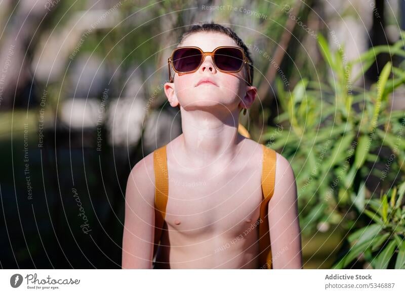 Stilvoller Junge mit Sonnenbrille in der Nähe von Pflanzen stehend Natur Sommer Urlaub selbstbewusst Kind Garten Brille nackter Torso grün Windstille jung Mode