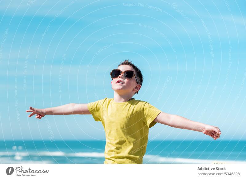 Junge mit ausgestreckten Armen genießt den Wind am Strand MEER Wasser Freiheit Blauer Himmel Kind Urlaub Glück Sonne ausdehnen froh Kindheit genießen positiv