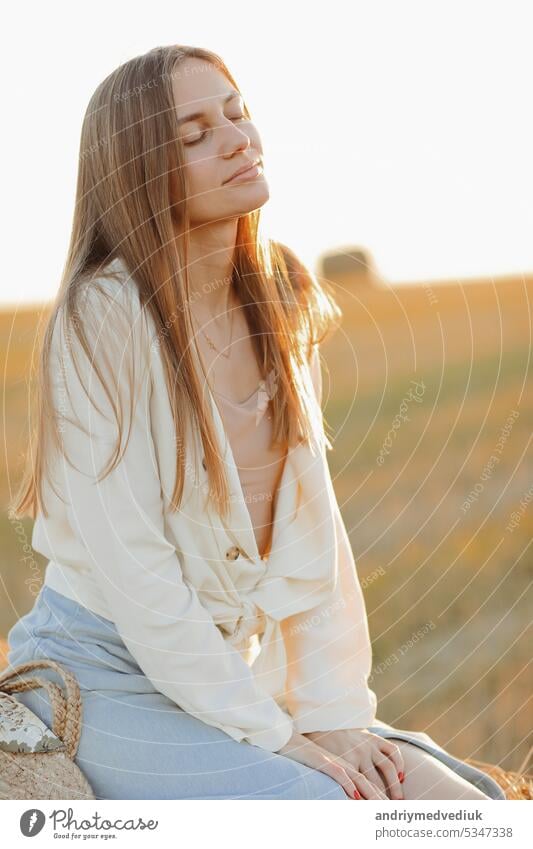 Schönes Porträt einer jungen Frau während des Sonnenuntergangs mit warmen gelben Sonnenstrahlen auf ihr Gesicht mit Strohballen auf dem Hintergrund ländlich