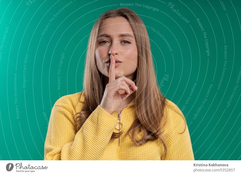 Lächelnde hübsche Frau mit Finger auf den Lippen - shhh, Geheimnis, Stille, blaues Studio fragen Hintergrund beißend charmant Nahaufnahme Konzept Verschwörung