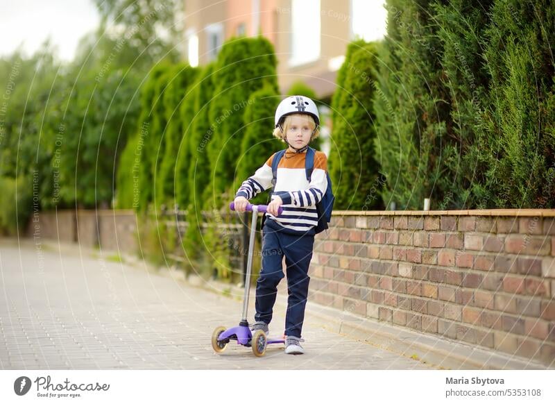 Kleiner Junge mit Schutzhelm fährt mit dem Roller zur Schule. Qualität schützen Ausrüstung für Sicherheit Kinder auf der Straße der Stadt. Zurück zu Schule Konzept.