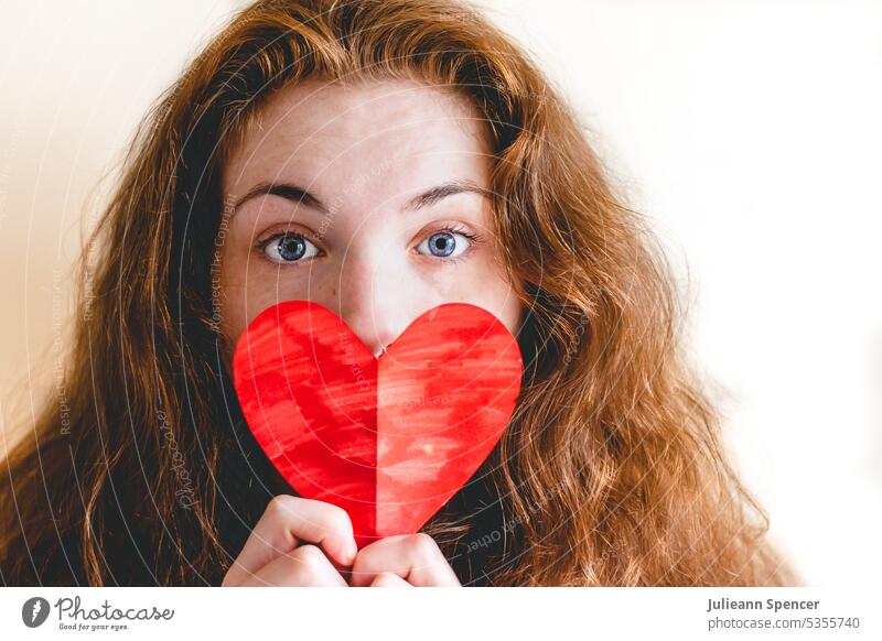 Red headed girl hält ausgeschnittene Herzform rot rothaarig rote Haare Behaarung rotes Herz ausschneiden herzförmig farbiges Papier eingefärbt bunt blaue Augen