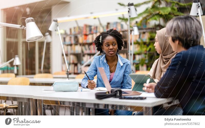 Multiethnische Gruppe von Studenten, die in einer Bibliothek sitzen und gemeinsam lernen echte Menschen Teenager Campus positiv Prüfung Wissen selbstbewusst