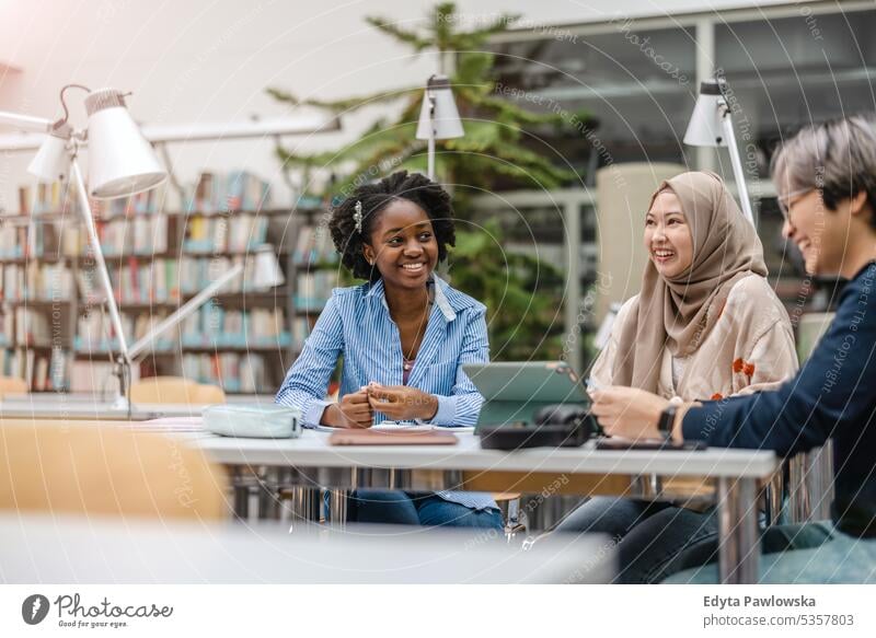 Multiethnische Gruppe von Studenten, die in einer Bibliothek sitzen und gemeinsam lernen echte Menschen Teenager Campus positiv Prüfung Wissen selbstbewusst