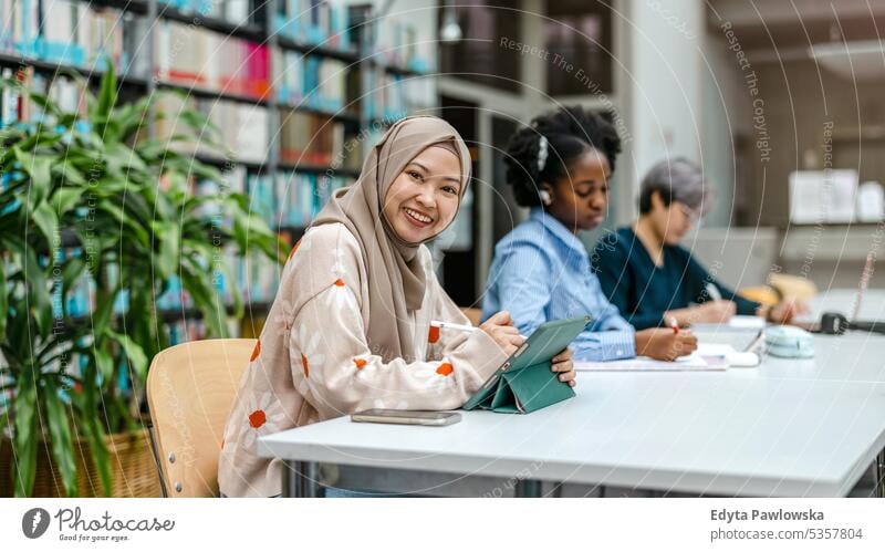 Multiethnische Gruppe von Studenten, die in einer Bibliothek sitzen und gemeinsam lernen echte Menschen Teenager Campus positiv Prüfung Wissen selbstbewusst