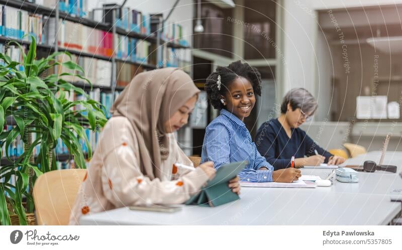 Multiethnische Gruppe von Studenten, die in einer Bibliothek sitzen und gemeinsam lernen echte Menschen Teenager Campus positiv Prüfung Wissen selbstbewusst