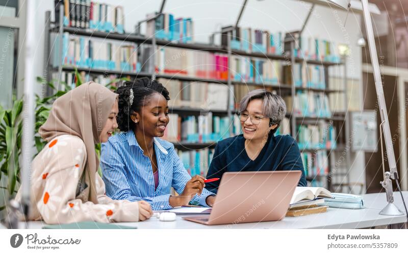 Multiethnische Gruppe von Studenten, die in einer Bibliothek sitzen und gemeinsam lernen echte Menschen Teenager Campus positiv Prüfung Wissen selbstbewusst