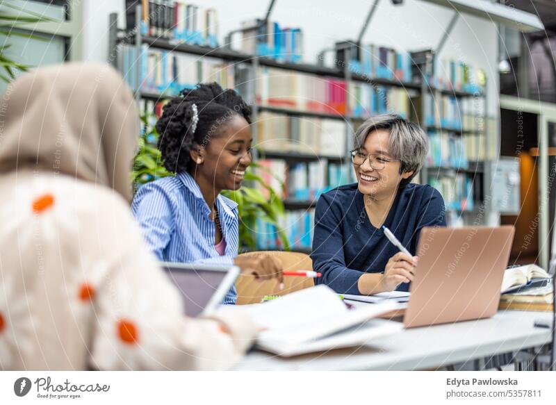 Multiethnische Gruppe von Studenten, die in einer Bibliothek sitzen und gemeinsam lernen echte Menschen Teenager Campus positiv Prüfung Wissen selbstbewusst