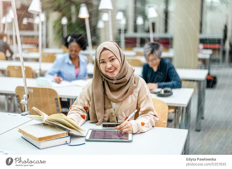 Multiethnische Gruppe von Studenten, die in einer Bibliothek sitzen und gemeinsam lernen echte Menschen Teenager Campus positiv Prüfung Wissen selbstbewusst