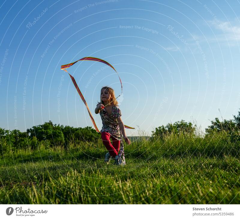 Lebhaftes Mädchen mit roter Hose tanzt mit Band auf der Wiese an einem sonnigen Tag Mädchen allein Mädchen tanzt Sommertag Kindheit Fröhlich Glück Sommerferien