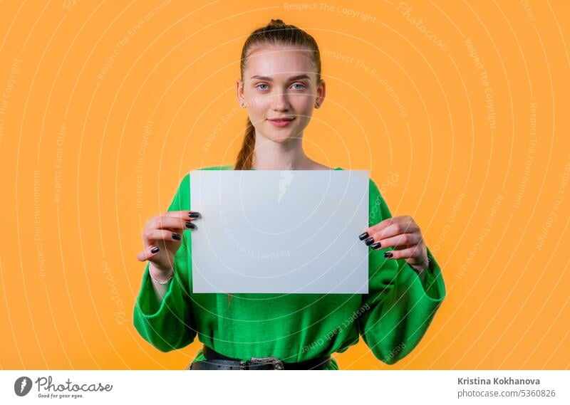 Junge Frau hält ein horizontales weißes A4-Papierplakat. Platz zum Kopieren. Anzeige Inserat Hintergrund Plakatwand blanko Holzplatte Heft Business