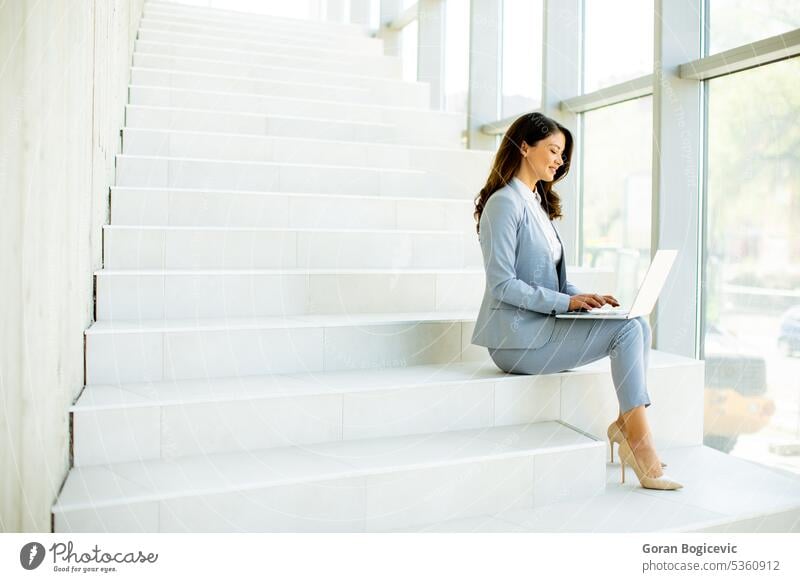 Junge Geschäftsfrau sitzt auf der Treppe im Büroflur und arbeitet am Laptop Internet modern Business Technik & Technologie Menschen Glück schön Mitteilung Frau